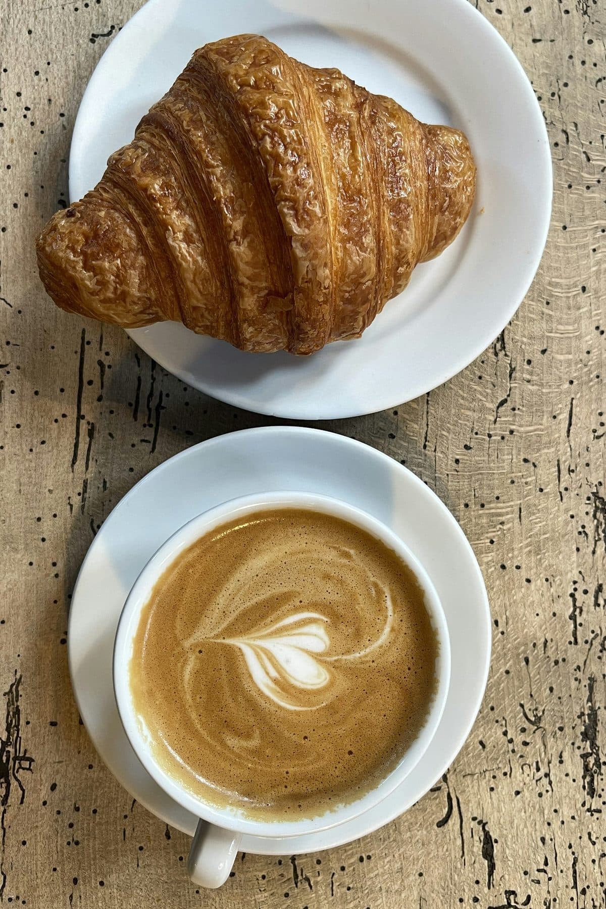 Una medialuna y un café con leche vistos desde arriba, sobre una mesa de madera.