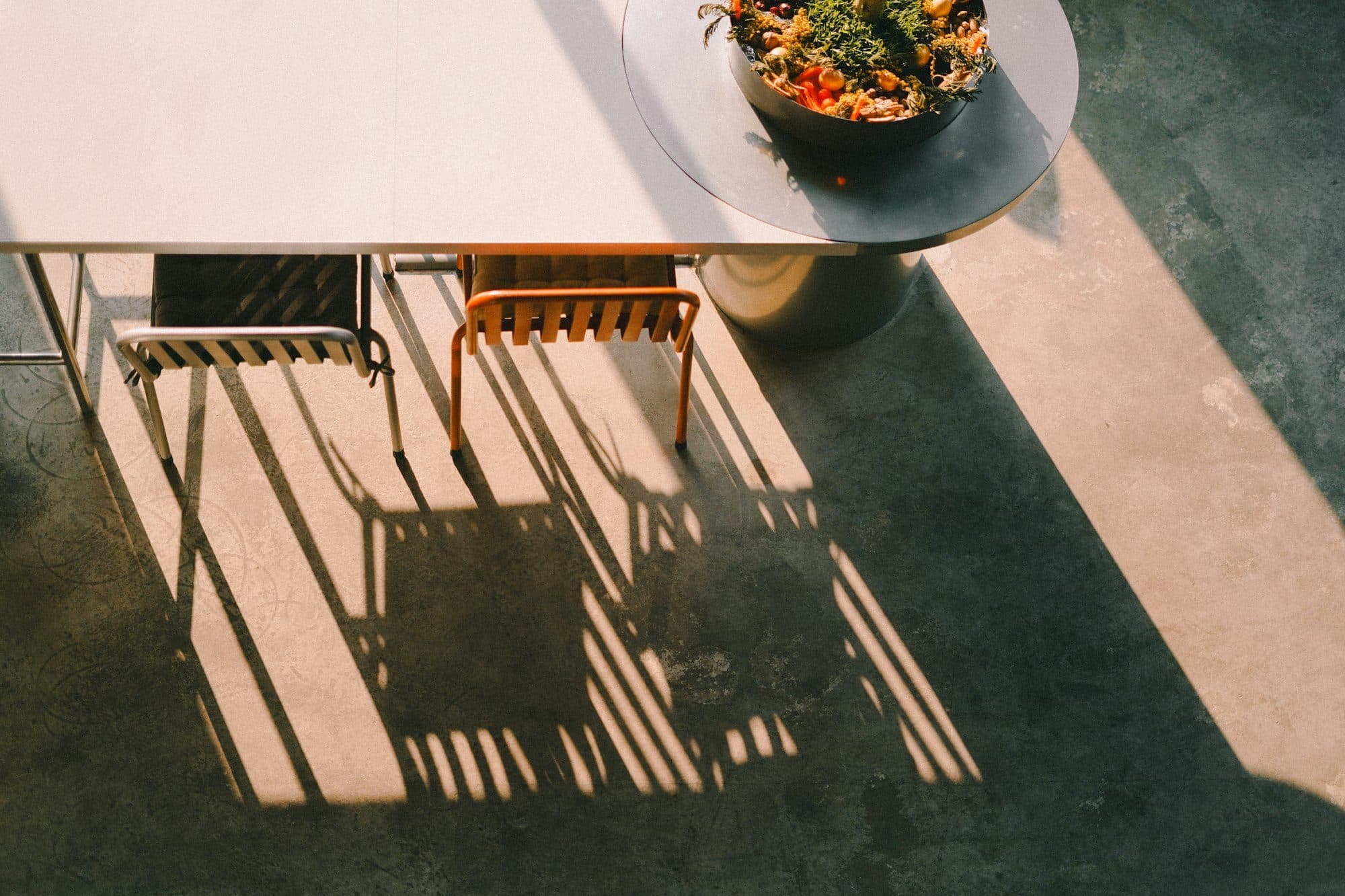 Una mesa con dos sillas vacías y el sol de la tarde estirando sus sombras en el piso.